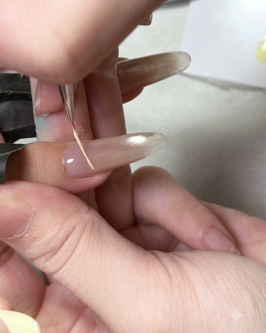 A fine detail brush applying glossy top coat onto a cured cat eye nail base.