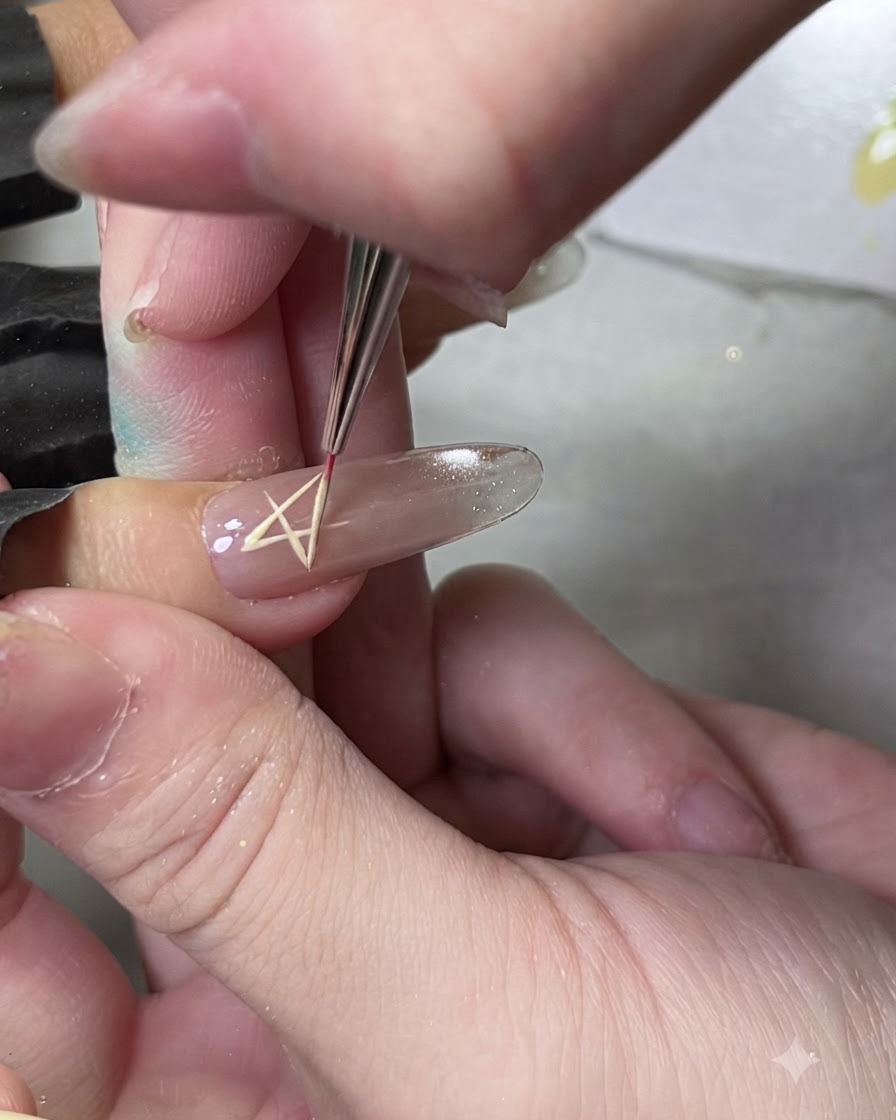 A fine liner brush drawing a star shape outline on a fingernail using yellow gel.