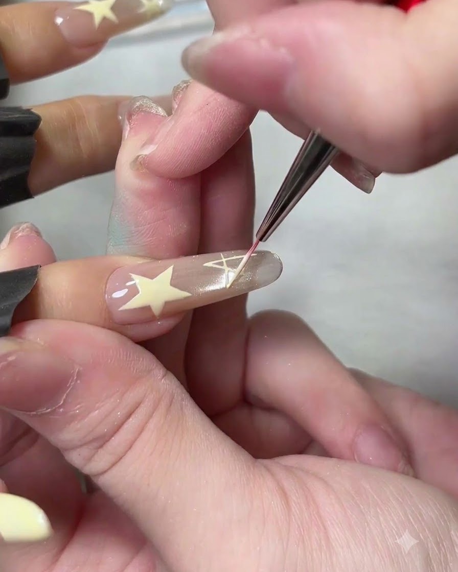 A fine liner brush drawing a white solid star design on a neutral-toned artificial nail.