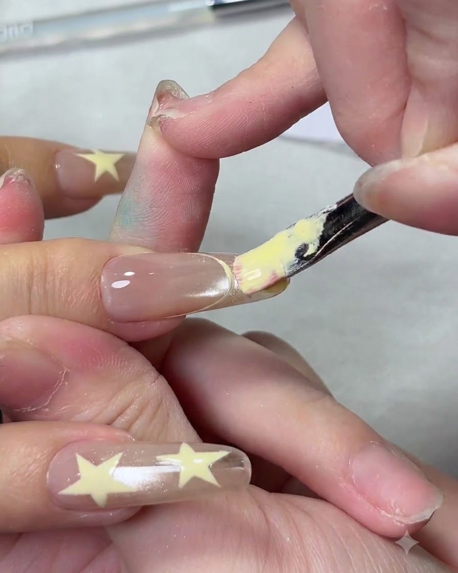 A flat nail brush applying a creamy yellow gel polish to the tip of a nail to create a French manicure.