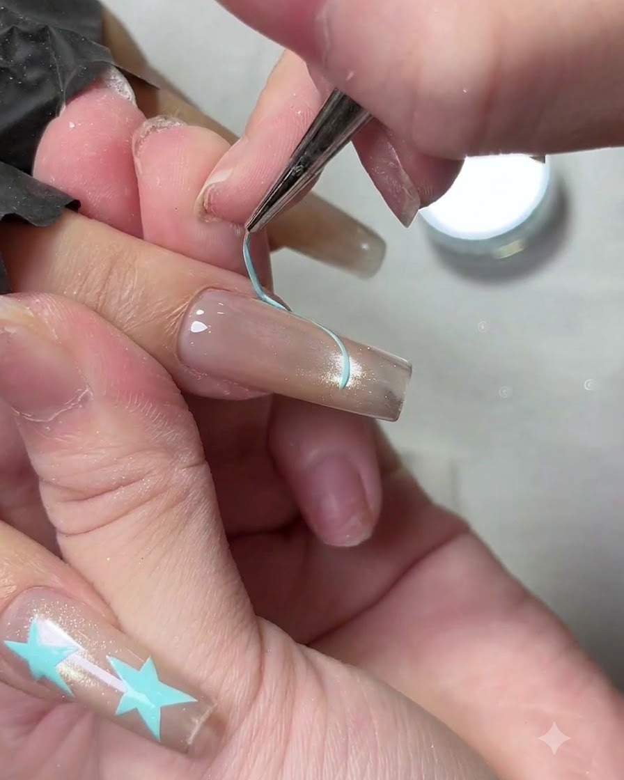 A fine liner brush outlining a light blue French tip smile line on a manicured fingernail.