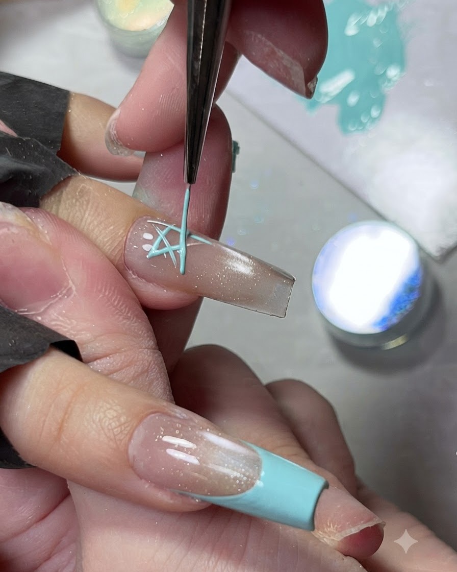 A fine liner brush painting a light blue star design on a glossy neutral nail extension.
