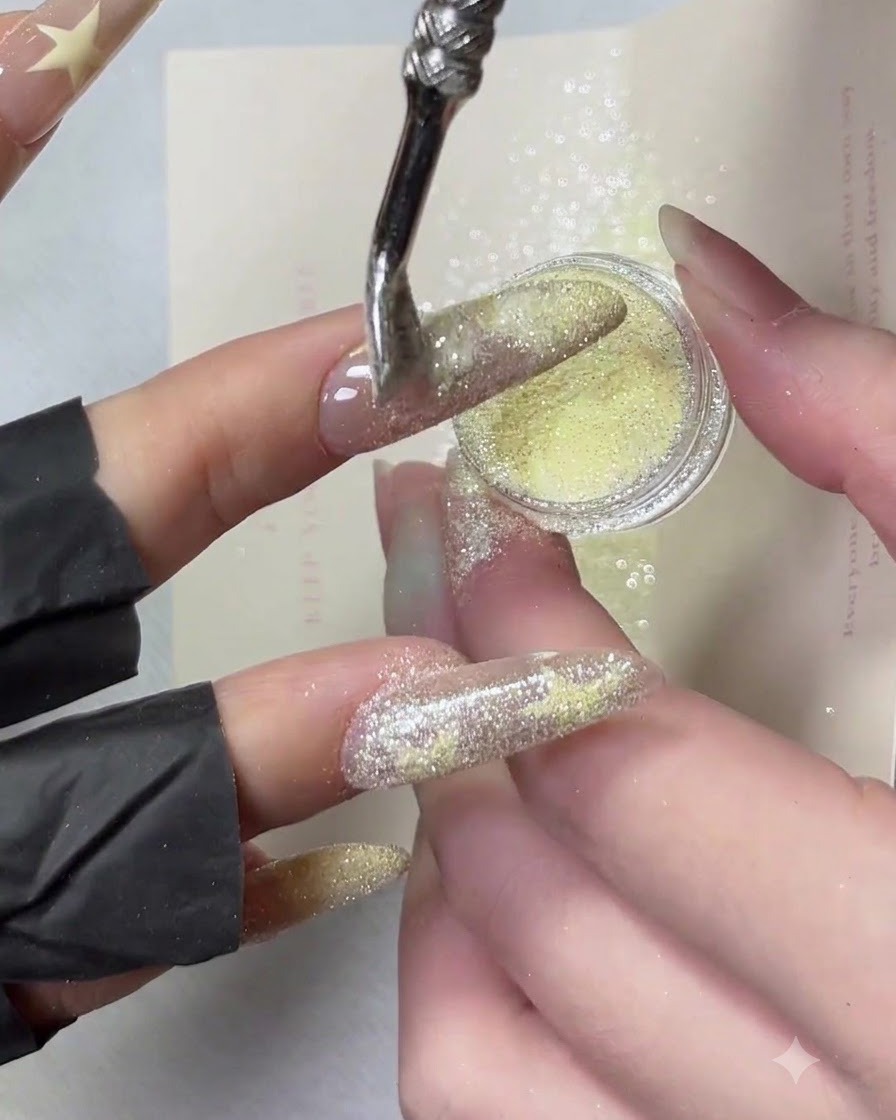 A hand tilted sideways while yellow crushed diamond powder is dusted over the edge of a French manicure tip.