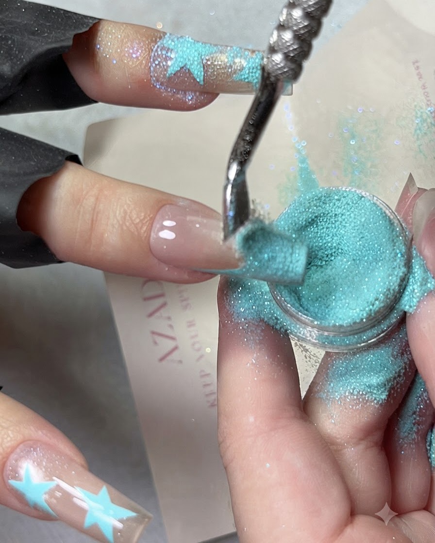 A close-up image showing baby blue crushed diamond powder being cascaded over a blue French tip design.