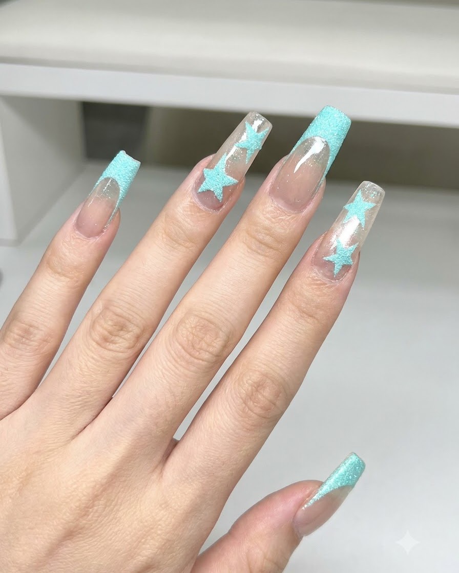 A dusting brush cleaning away blue glitter powder from long square nails featuring blue star art and French tips.