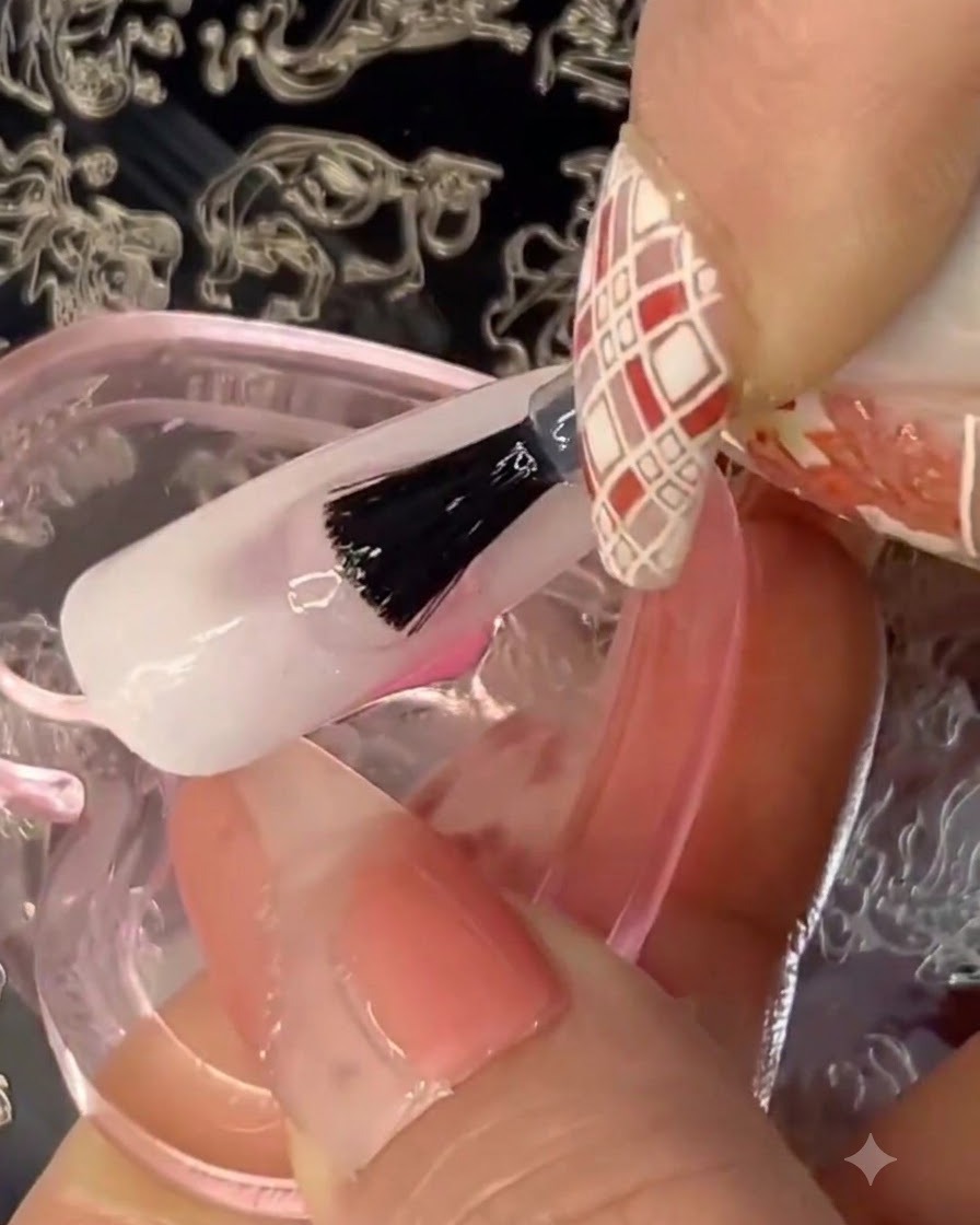 A pair of tweezers placing small gold foil flakes onto a tacky, translucent gel base on a practice nail.