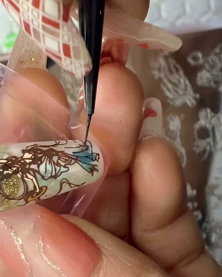 A clear nail stamper pressing down onto a decorated nail tip to transfer a detailed brown line art figure.