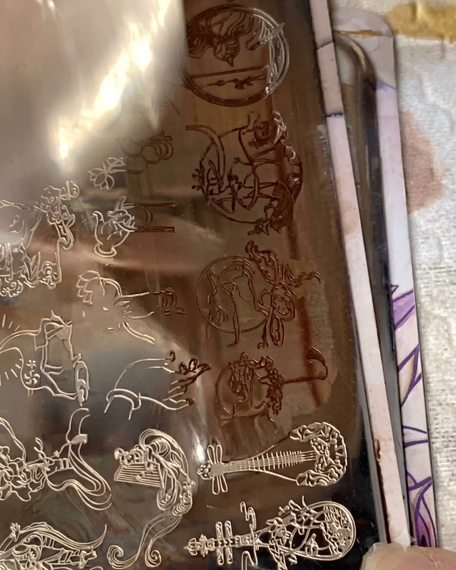 A nail stamper placing a detailed tiny character transfer onto the pinky fingernail.