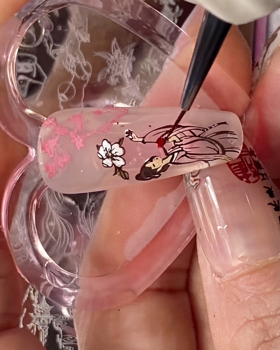 A detail brush applying red blooming liquid onto the dress portion of the stamped figure on a nail tip.