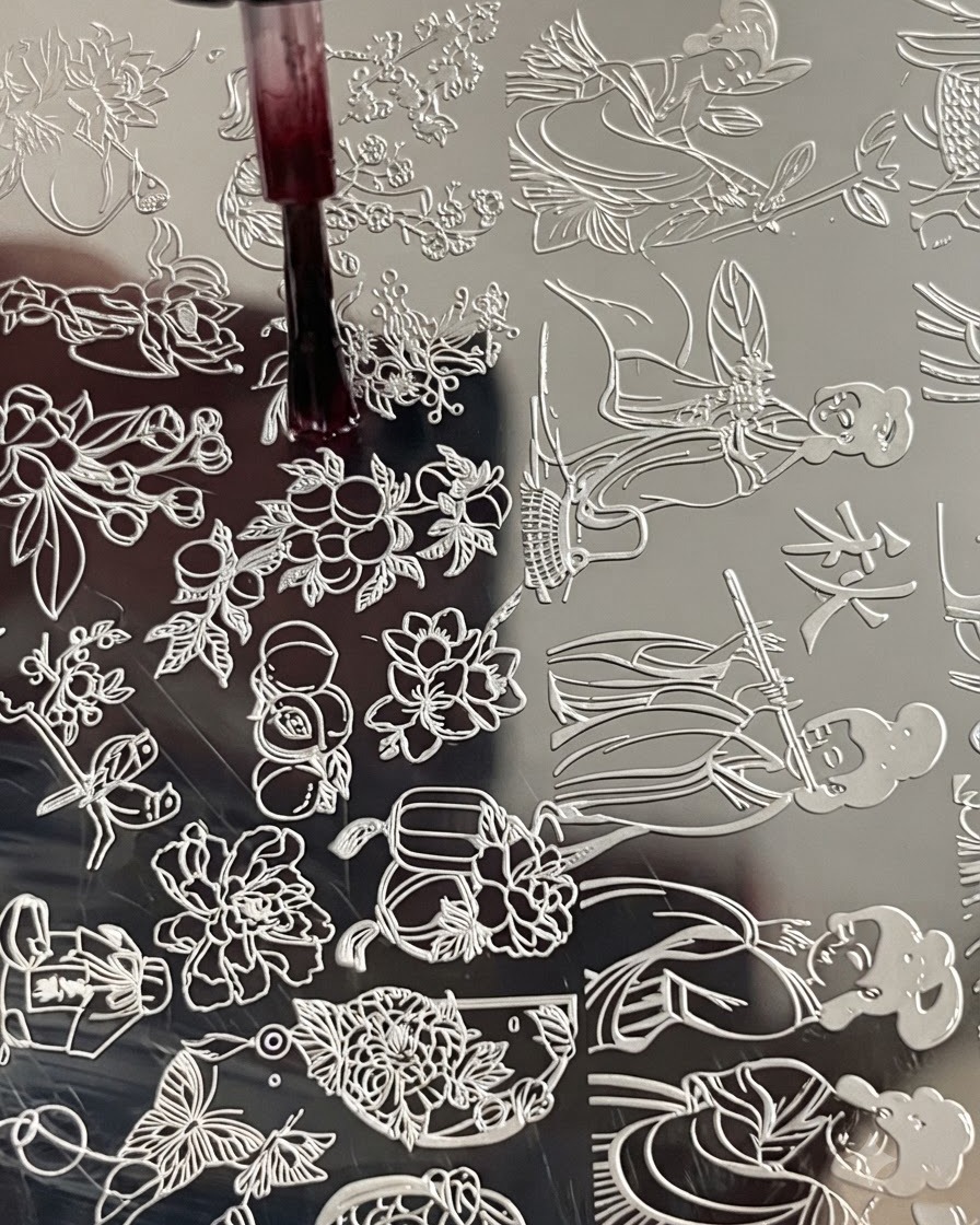 A brush applying blooming liquid onto a floral engraving on a metal stamping plate.
