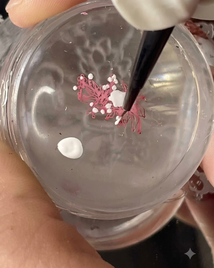 A clear silicone stamper holding a transferred floral stamping design while white dots are being added with a fine brush.