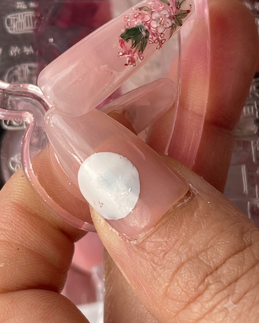 A finished nail tip with a pinkish base and delicate floral art, shown alongside a separate nail sample.