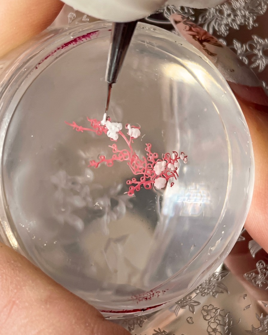 A fine brush picking up detailed branch patterns from a stamping plate using blooming liquid.