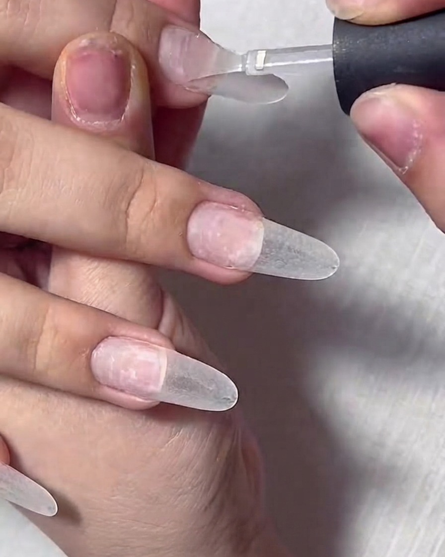 A close-up of a brush applying clear base gel to a prepped natural fingernail.