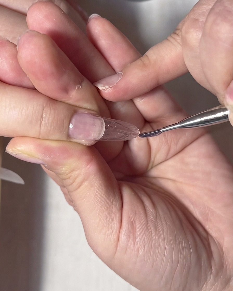 A fine liner brush adjusting clear gel near the cuticle and side edges of the nail.
