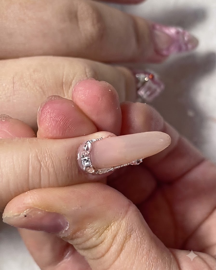 Close-up of a finished pinky fingernail beautifully decorated with tiny sparkling rhinestones along the cuticle edge.