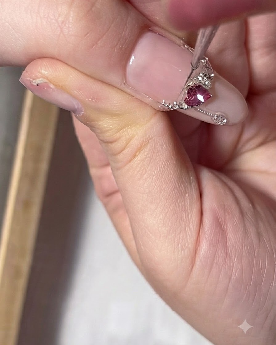 A close-up of a thumb nail featuring a red oval gem arranged to look like a necklace pendant.