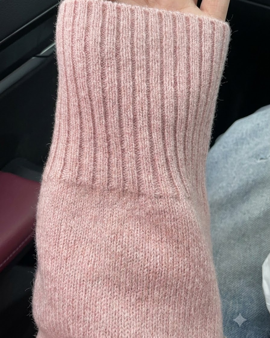 A vertical hand position showing nail length paired with the pink knit sweater sleeve.